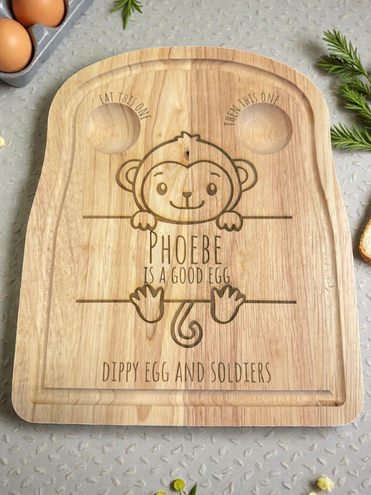 Wooden cutting board with monkey design and text on a gray surface with eggs.