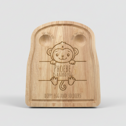 Wooden cutting board with monkey design and text on a gray surface with eggs.
