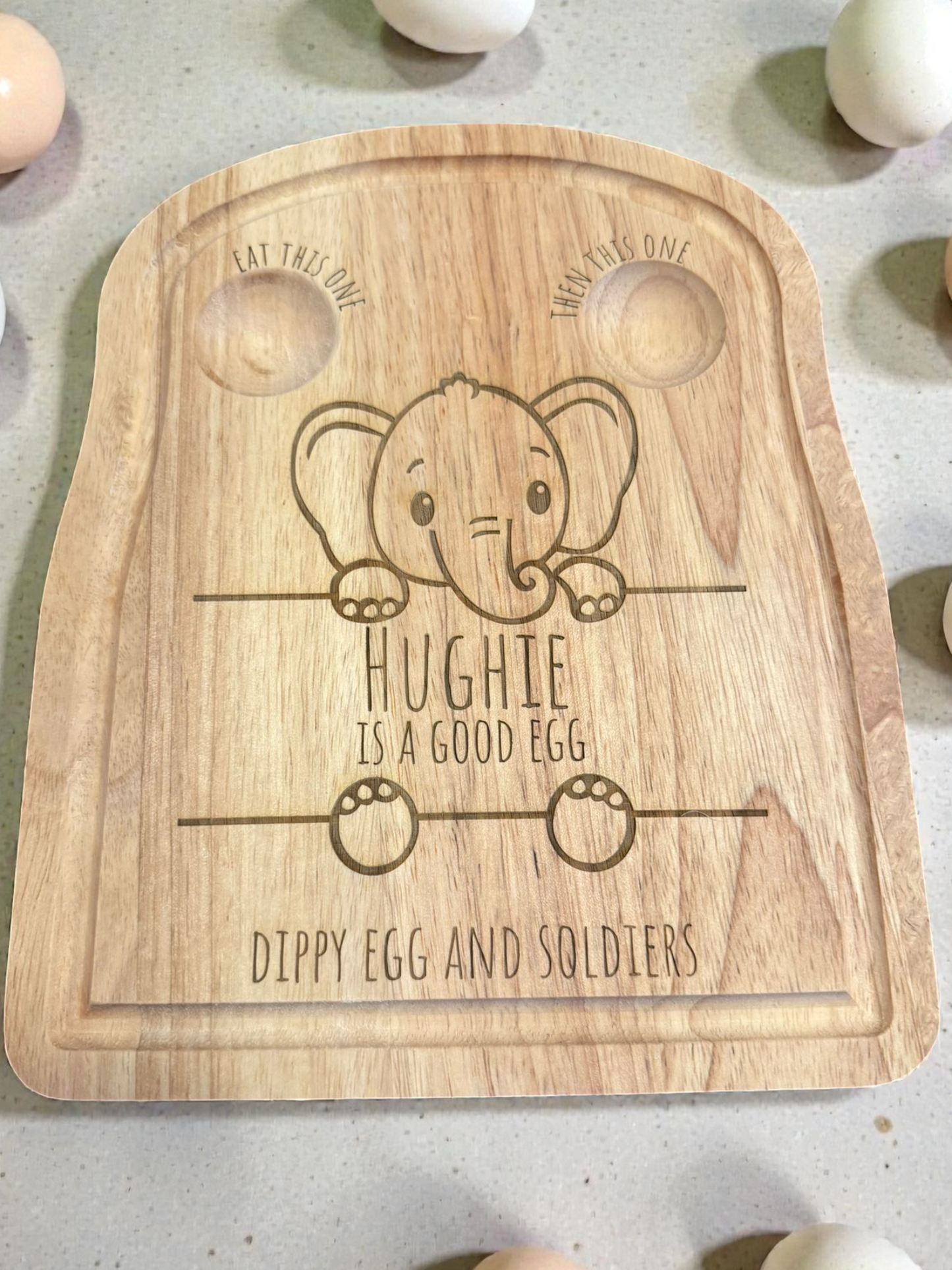 Wooden egg tray with engraved elephant design and text on a concrete surface with eggs around.