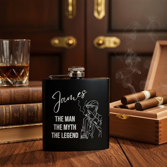 Black flask with 'James: The Man, The Myth, The Legend' text and smoking man illustration on a wooden surface.